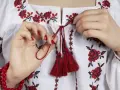 Manos atando cordones rojos en una blusa blanca con **bordado digital** de flores rojas y negras.