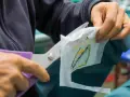 Manos cortan con tijeras un parche bordado sobre tela estabilizadora, preparándolo para ser cosido.