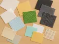 Variedad de retazos de tela, algunos con estampados de puntos y cuadros, otros lisos en tonos pastel y grises. Un tejido fuerte empleado para entretelas.