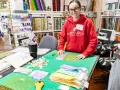 Mujer sonriente en tienda de telas, rodeada de retazos y herramientas de costura.