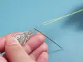 Manos usando un enhebrador de agujas para pasar hilo amarillo por el ojo de una aguja.