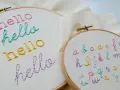 Bastidores de bordado con la palabra "hello" en varios colores y un abecedario completo. Ideales para practicar letras para bordar nombres.