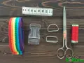 Herramientas para hacer un collar para perro: cinta métrica, cinta de arcoíris, hebilla, anillas, tijeras y hilo rojo.
