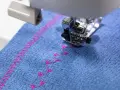 Máquina de coser bordando un patrón decorativo en **tejidos de algodón** azul con hilo rosa.