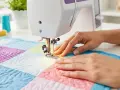 Manos cosiendo un quilt colorido con máquina de coser. La tela waterproof se ve resistente y lista para cualquier proyecto.