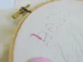 Bastidor con tela y un hilo rosa comenzando a bordar letras.