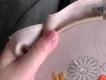 Mano sujetando un bastidor de bordar con lino para bordar. Se aprecian flores a medio bordar en tonos grises, naranjas y amarillos.