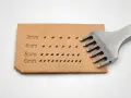 Un punzón de cuero con dientes metálicos crea filas de agujeros en una tira de cuero, mostrando diferentes tamaños de puntadas.