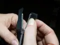 Manos sujetan una cremallera negra, alineando los dientes para coser cremallera a mano.