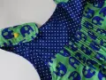 Detalle de un vestido infantil con estampado de elefantes azules sobre fondo verde. El cuello tiene un detalle de lunares azules y un botón amarillo en forma de corazón. Un adorable **patrón ranita bebé**.