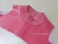 Detalle de camiseta rosa con bordado a mano en el cuello, creando un diseño delicado y único.