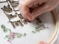 Mano deshaciendo puntadas de un bordado en tela blanca con aro. Aprende como quitar un bordado de una prenda.