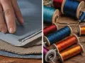 Mano sobre telas azules y marrones, junto a carretes de hilo de colores vibrantes, listos para aprender como coser un agujero a mano.