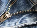 Primer plano de una cremallera atascada con tela de mezclilla azul. El tirador metálico muestra la marca "YTR".