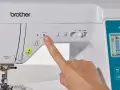 Dedo presionando botón en máquina de coser Brother. Guía para como elegir máquina de coser.