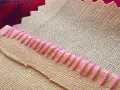 Detalle de tela beige con puntada de hilo rosa formando un borde decorativo.