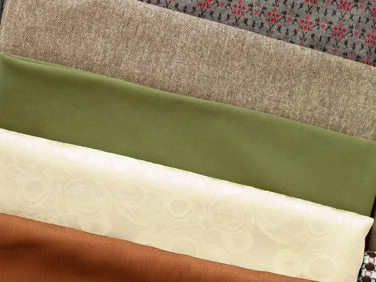 Variedad de tipos de tela apiladas: gris con patrón, beige texturizado, verde liso, crema con relieve floral y marrón.