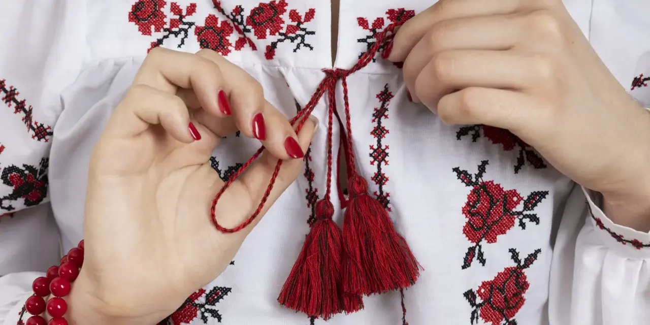 Manos atando cordones rojos en una blusa blanca con **bordado digital** de flores rojas y negras.