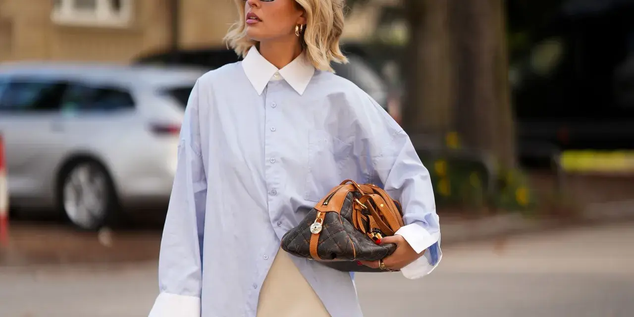 Mujer con camisa oversize azul, falda lencera de encaje y bolso de diseño. Un look para tunear ropa de mujer con estilo.