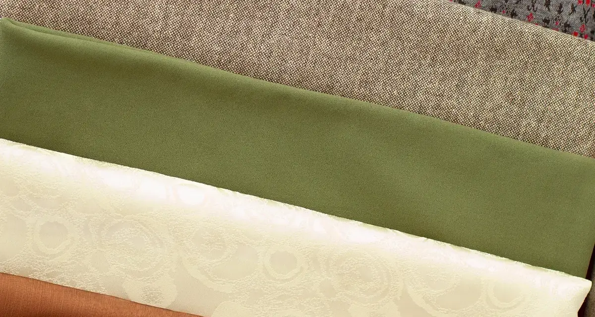 Variedad de tipos de tela apiladas: gris con patrón, beige texturizado, verde liso, crema con relieve floral y marrón.