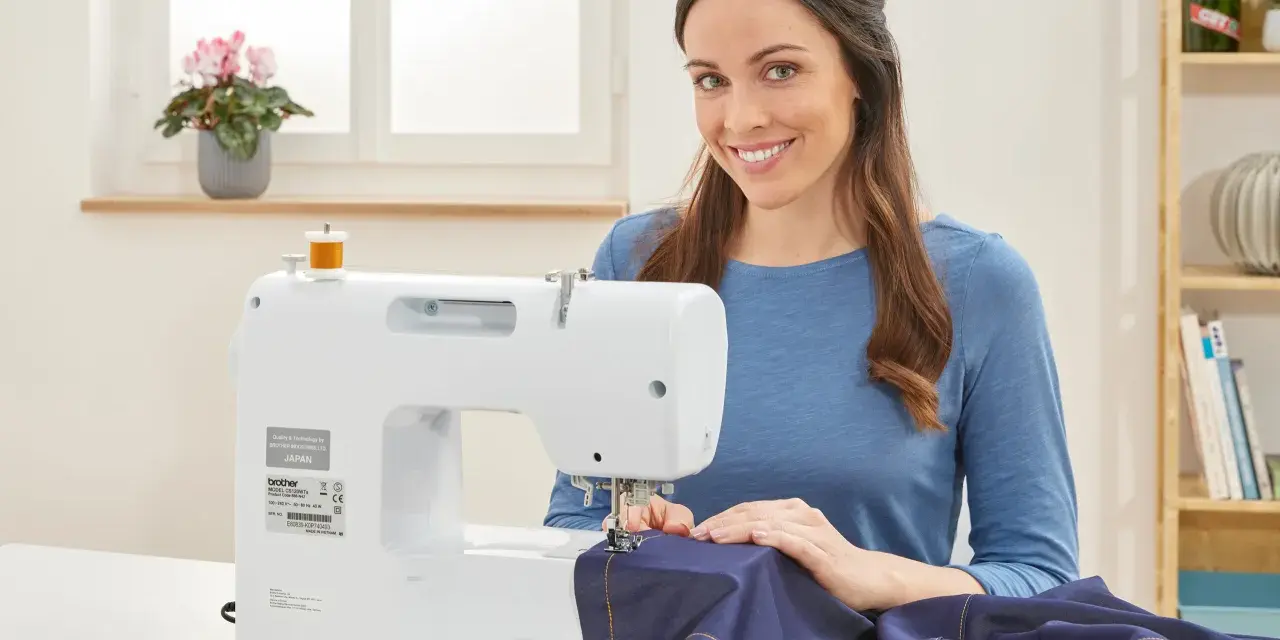 Mujer sonriente cosiendo a maquina una tela azul.