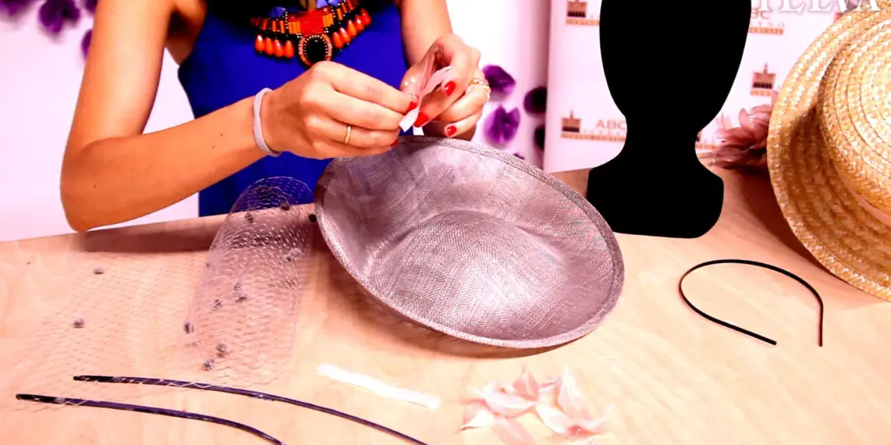 Manos creando un tocado con diadema. Materiales: velo, plumas, base de tocado y diadema.