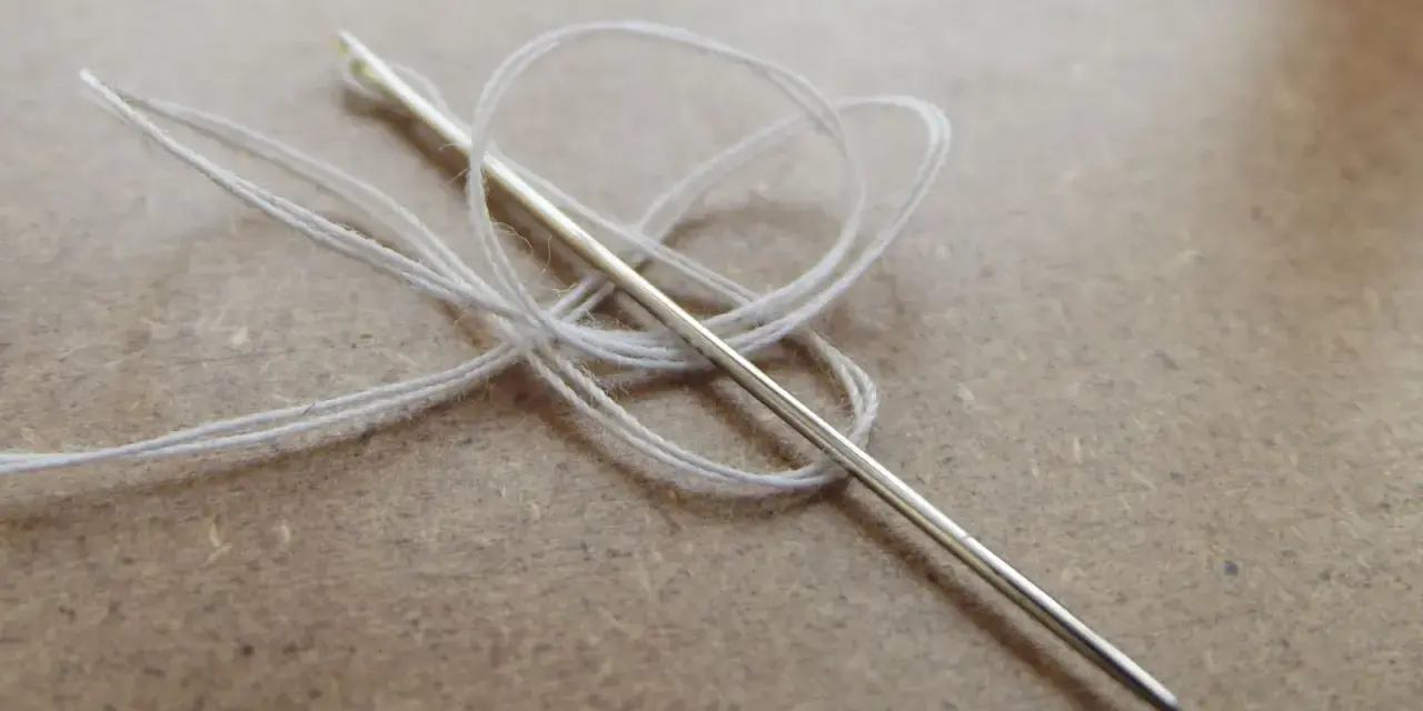 Aguja con hilo blanco enredado, lista para coser a punto de lado.