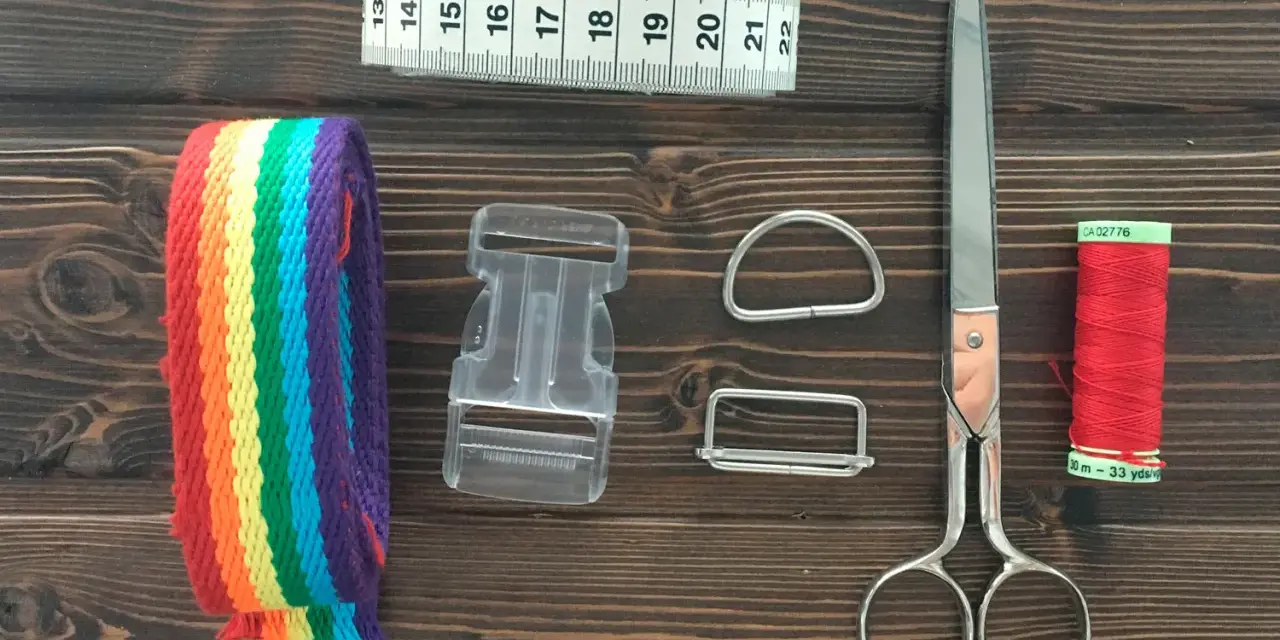 Herramientas para hacer un collar para perro: cinta métrica, cinta de arcoíris, hebilla, anillas, tijeras y hilo rojo.