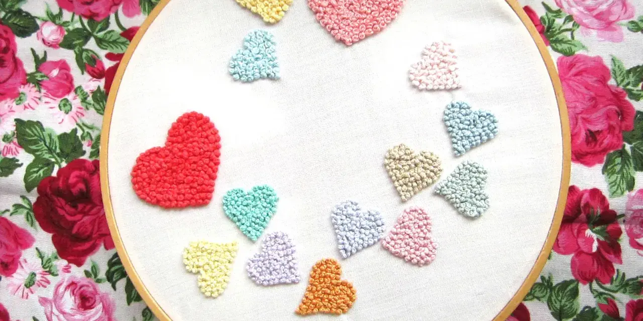 Un aro de bordar muestra un montón de corazones bordados de colores, como un arcoíris de amor.