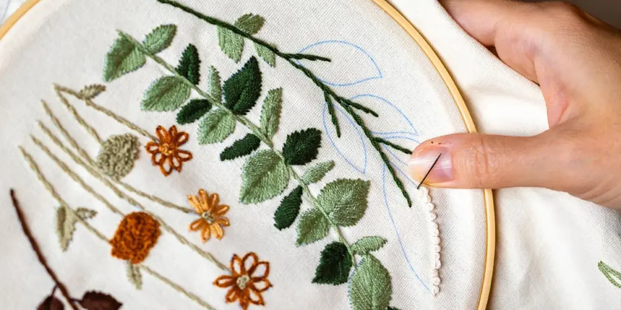 Manos creando bellas ideas para bordar: hojas verdes y flores naranjas en tela, con aguja e hilo listos para continuar.
