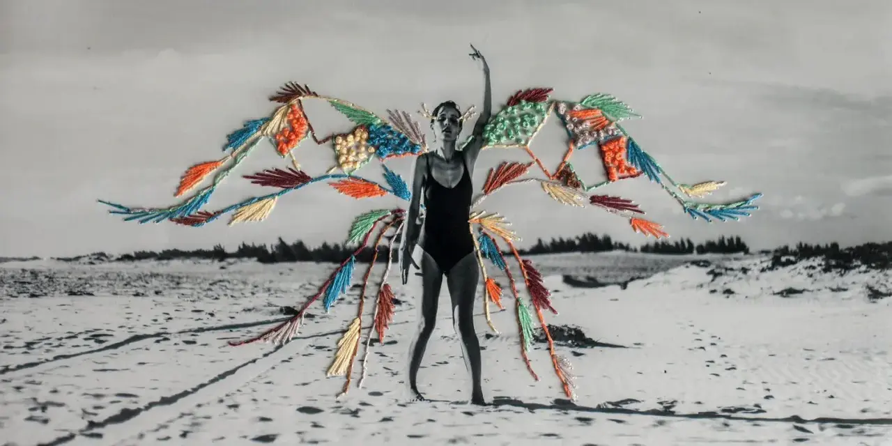 Mujer en traje de baño con alas de bordado de fotos coloridas sobre un paisaje de playa desértica.