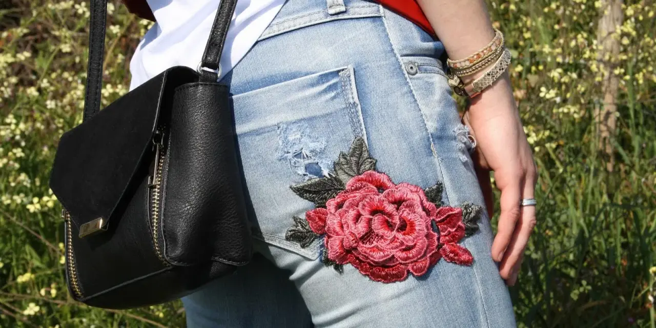 Detalle de unos pantalones vaqueros con un llamativo bordado de rosa roja, perfectos para tunear tus vaqueros y darle un toque único.