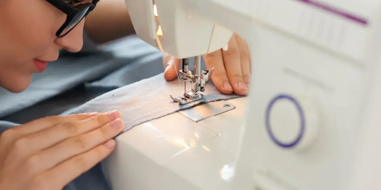 Mujer con gafas concentrada en sus proyectos de costura, cosiendo tela azul en una máquina de coser.