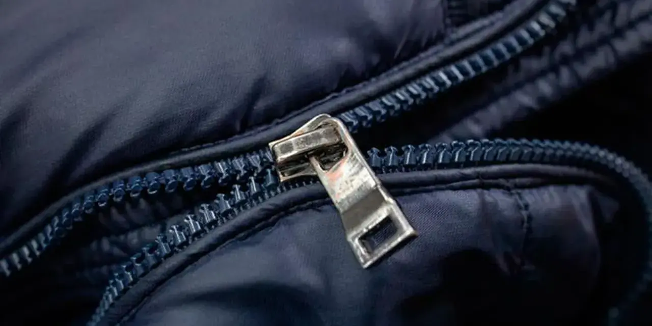 Enganche cremallera roto en chaqueta azul marino. El tirador metálico está desprendido, dejando la cremallera inutilizable.