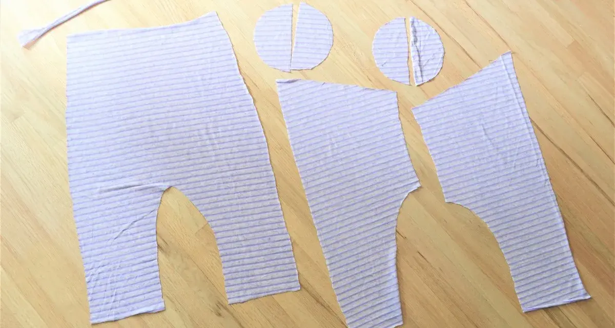 Piezas de tela a rayas lilas, listas para coser un patrón de peto para bebé.