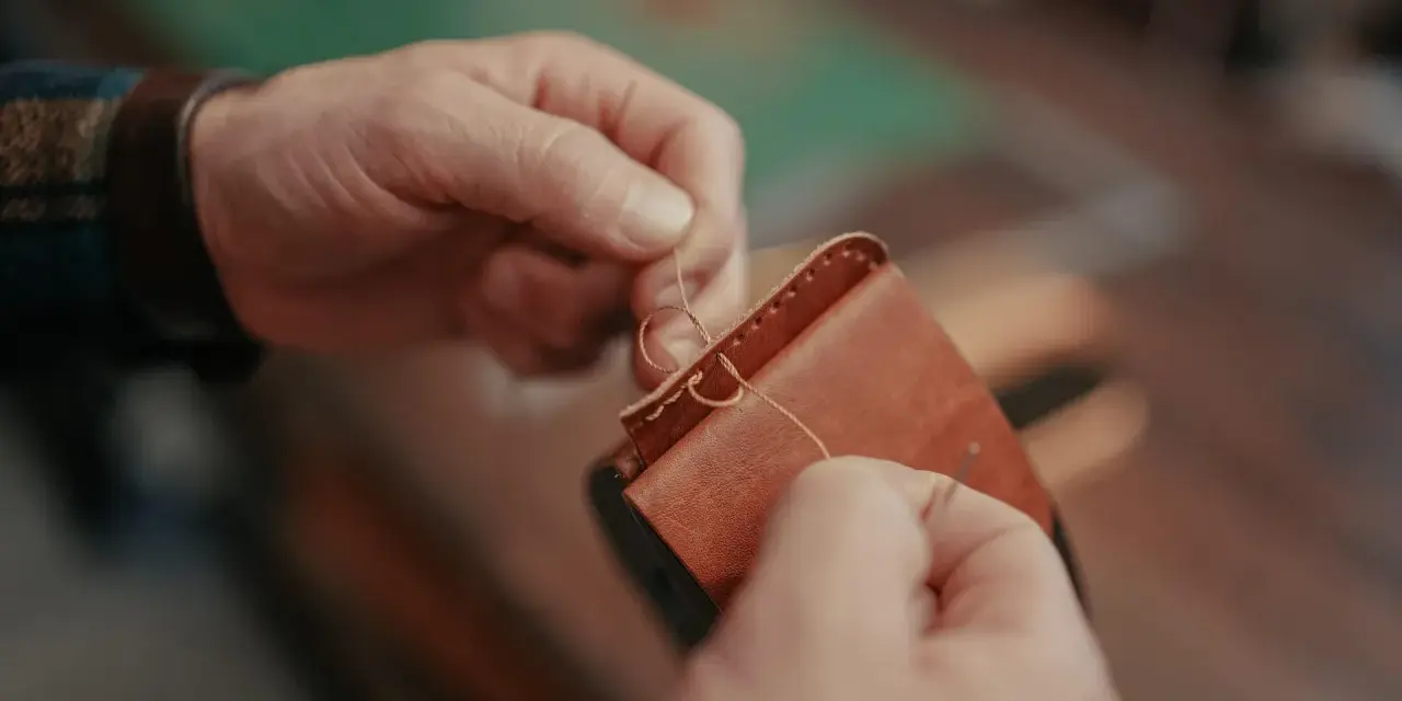 Manos cosiendo a mano un monedero de cuero. Se aprecian los detalles de los tipos de costuras de cuero a mano.
