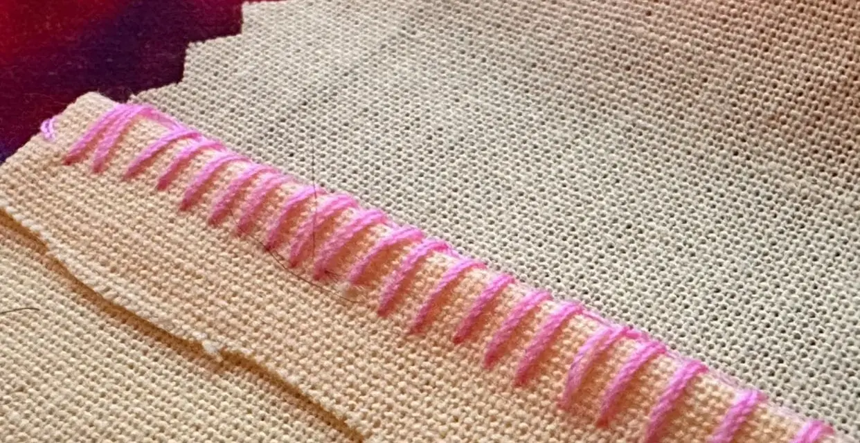 Detalle de tela beige con puntada de hilo rosa formando un borde decorativo.