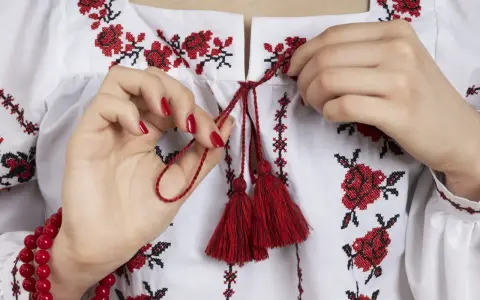 Manos atando cordones rojos en una blusa blanca con **bordado digital** de flores rojas y negras.