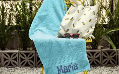 Toalla turquesa con el nombre "María" bordado, lista para la playa.
