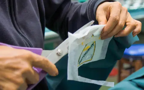 Manos cortan con tijeras un parche bordado sobre tela estabilizadora, preparándolo para ser cosido.