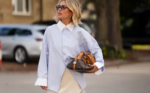 Mujer con camisa oversize azul, falda lencera de encaje y bolso de diseño. Un look para tunear ropa de mujer con estilo.