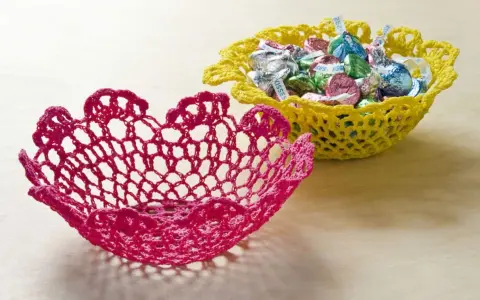 Dos cuencos de ganchillo, uno rosa y otro amarillo lleno de caramelos. Aprende como dar rigidez a una tela para crear estas piezas decorativas.