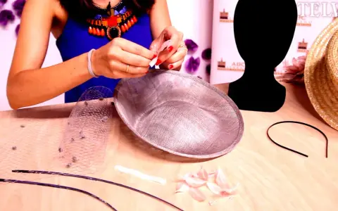 Manos creando un tocado con diadema. Materiales: velo, plumas, base de tocado y diadema.