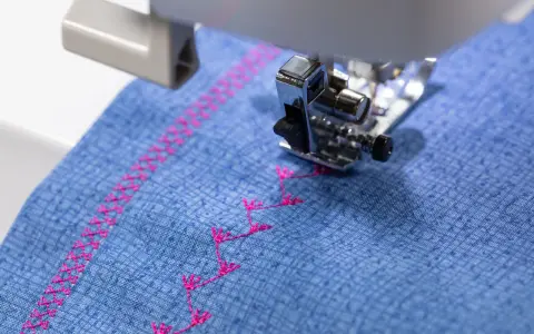 Máquina de coser bordando un patrón decorativo en **tejidos de algodón** azul con hilo rosa.