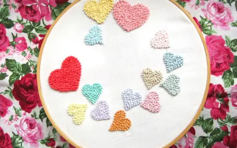 Un aro de bordar muestra un montón de corazones bordados de colores, como un arcoíris de amor.