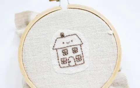 Bordado de una casita sonriente sobre papel para bordar que se deshace con el agua.