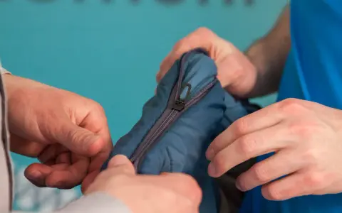 Manos intentan arreglar pistón cremallera de un saco de dormir azul.