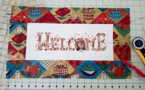 Un bordado de "Welcome" con un pavo, listo para enmarcar telas bordadas con un diseño otoñal.