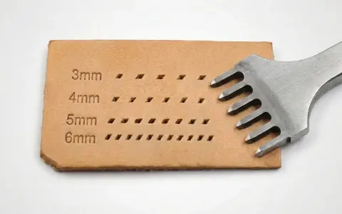 Un punzón de cuero con dientes metálicos crea filas de agujeros en una tira de cuero, mostrando diferentes tamaños de puntadas.