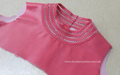 Detalle de camiseta rosa con bordado a mano en el cuello, creando un diseño delicado y único.